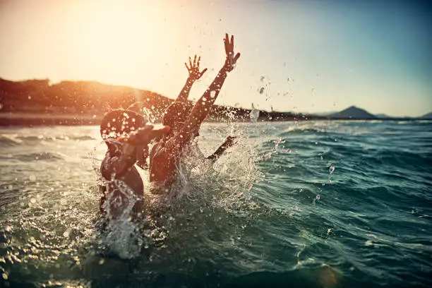 Children are having splashing fun in sea on summer sunset.  Children are aged 6 and 11.
