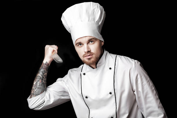 istock Young bearded man chef In white uniform holds  knife on  black background 689948496