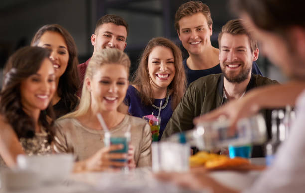 Drinks and a show Shot of a happy group of friends having drinks at a bar together cocktail bar busy stock pictures, royalty-free photos & images