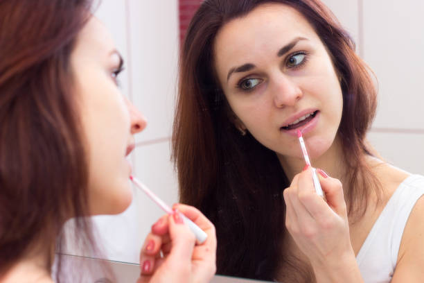 istock Young woman lip glossing in bathroom 689955526
