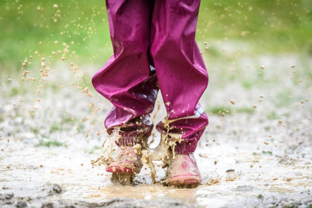 istock Children in rubber boots and rain clothes jumping in puddle. 689955778