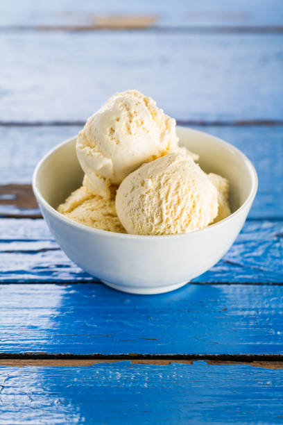 cucharadas de sabroso hielo de vainilla en un tazón sobre la mesa rústica de madera azul. closeup. - gelato cream ice cream ice fotografías e imágenes de stock