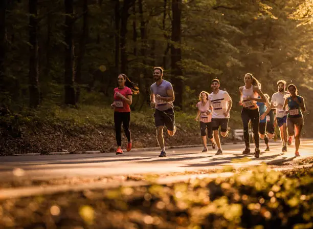 Large group of athletes running a marathon in nature at sunset.