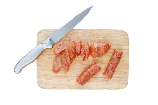 Sliced Chinese sausages on chopping block with knife isolated on white background.