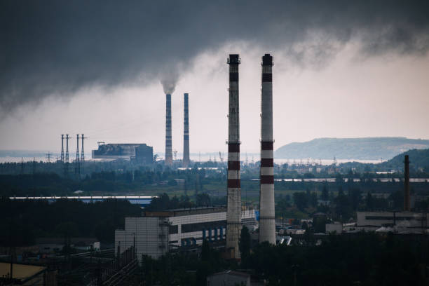 altas torres, fumaça e dramática céu acima zona industrial perto da cidade - smog city pollution town - fotografias e filmes do acervo