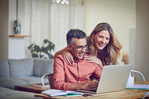 Shot of a mature woman leaning on her husband while he works on his laptop