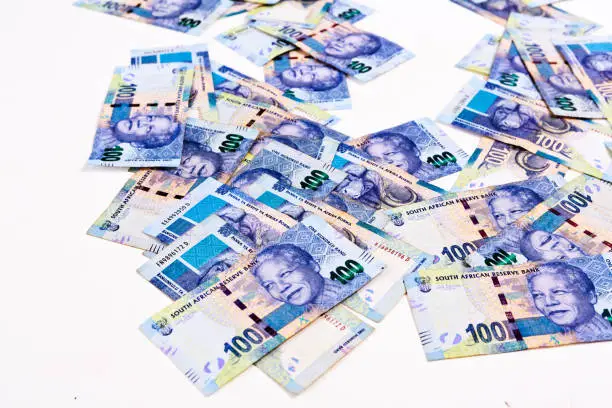 A background of many South African One Hundred Rand banknotes spread out on white.