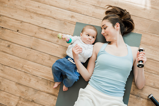 Top view of mother with baby boy lying on floor and playing with dumbbells
