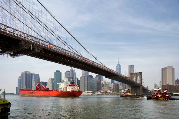 cargo ship and tug boat under brooklyn bridge, New York City stock photo