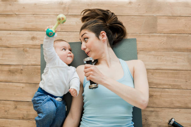 mother with baby boy lying on floor and playing with dumbbells Top view of mother with baby boy lying on floor and playing with dumbbells exercise mat photos stock pictures, royalty-free photos & images