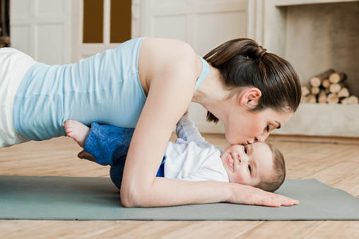 Side view of woman doing plank exercise and kissing her son