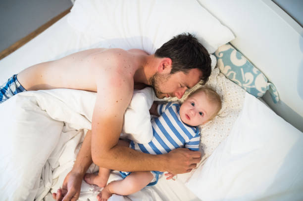 istock Baby boy lying in bed, his father hugging him 689998628