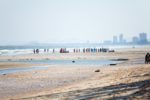 View southwards beach of Cha-Am towards Hua Hin in Thailand. On beach is a large group of young thai men. In background are hotels of northern Hua Hin.