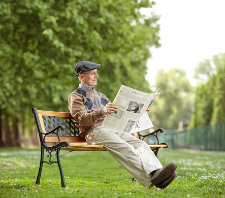 Senior sitting on a bench and reading a newspaper in the park