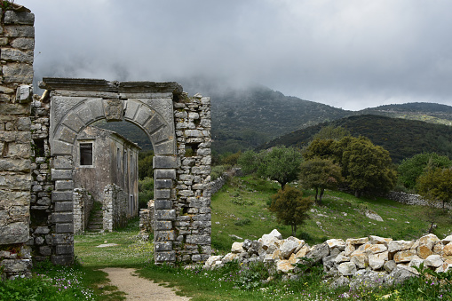 The old abandoned stone-built village of Perithia high in Pantokrator Mountain, Corfu Island, Greece. Nostalgic spring day in the spooky village. Clouds creep over the mountain slopes around the village