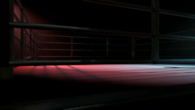 Boxing ring surrounded by ropes spotlit in either opposing corner