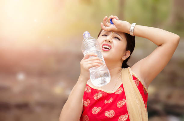 Woman suffers from heat of strong sunlight, Blur background Young Indian woman holding water bottle during warm sunny day. hyperthermia photos stock pictures, royalty-free photos & images