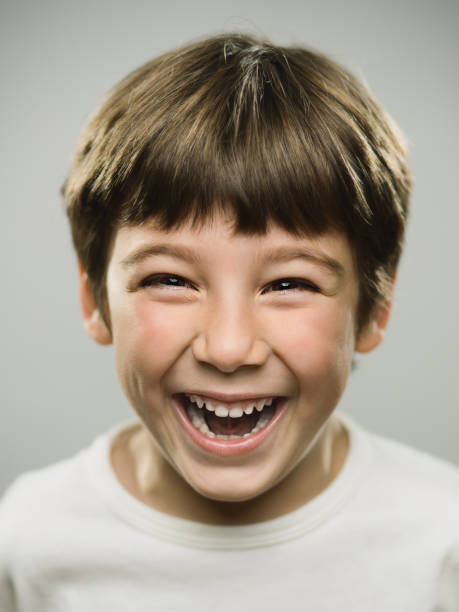 Cute little boy laughing in studio Close up portrait of cute little boy laughing against gray background. Vertical shot of real kid looking excited in studio. Photography from a DSLR camera. Sharp focus on eyes. mischief photos stock pictures, royalty-free photos & images