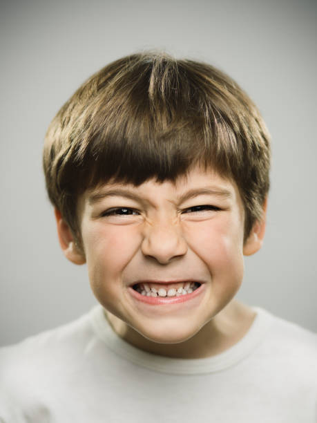 Closeup of little boy looking angry Closeup portrait of little boy looking angry against gray background. Vertical shot of real kid with angry facial expression in studio. Photography from a DSLR camera. Sharp focus on eyes. clenching teeth stock pictures, royalty-free photos & images