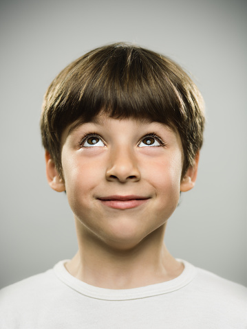 Close up portrait of cute little boy looking up. Vertical shot of real young boy against gray background in studio. Photography from a DSLR camera. Sharp focus on eyes.