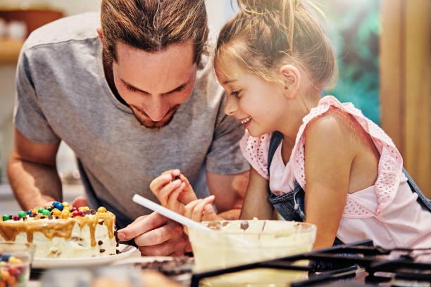 I'll decorate it Shot of a handsome young man baking a cake with his daughter decorating a cake photos stock pictures, royalty-free photos & images