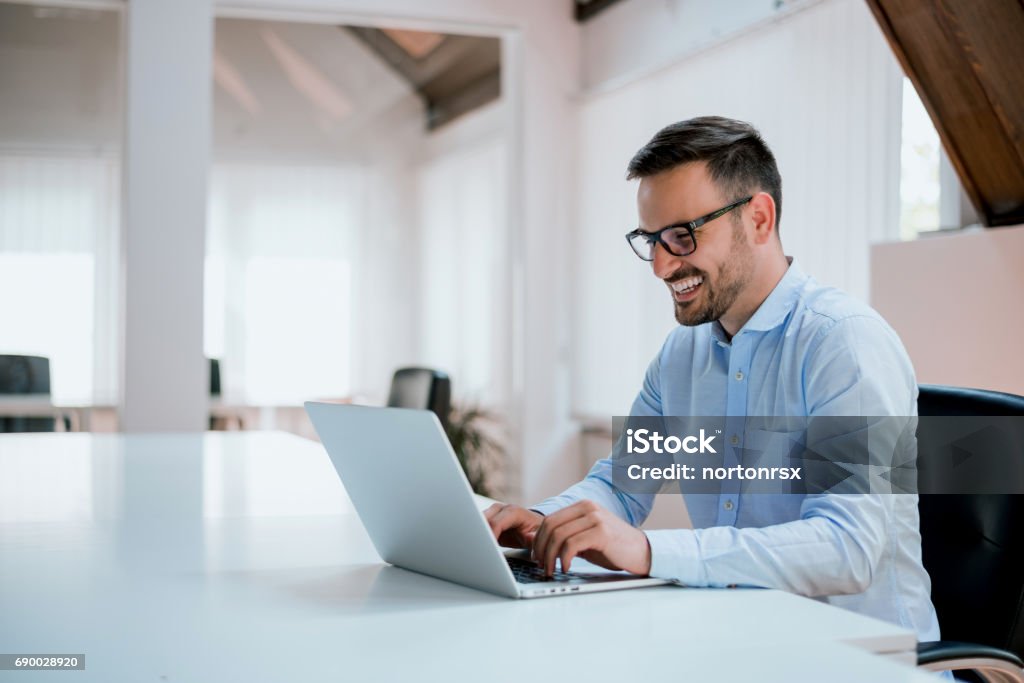 Portrait of young man sitting at his desk in the office Laptop Stock Photo