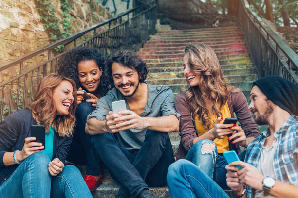 Friendship and networking Multi-ethnic group of friends with smart phones sitting on a staircase street friends stock pictures, royalty-free photos & images