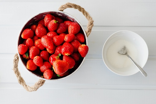 Fresh red strawberries in white bowl and sugarbowl