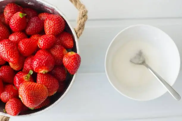 Fresh red strawberries in white bowl and sugarbowl on white wooden table in kitchen