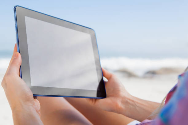istock Woman sitting on beach in deck chair using tablet pc 690035550