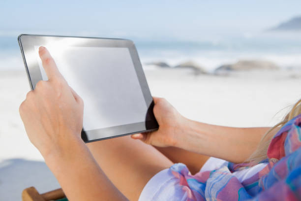 istock Woman sitting on beach in deck chair using tablet pc 690035578