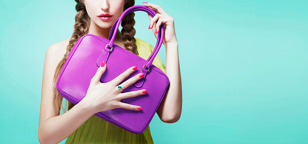 Young girl holding purple leather handbag purse. isolated on bright aqua blue background. Fashion item image.