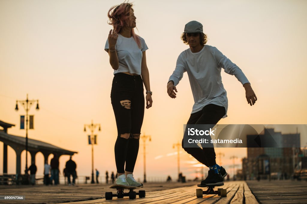 Teenage couple riding longboards on the boardwalk Young teenage couple with longboards Skateboarding Stock Photo