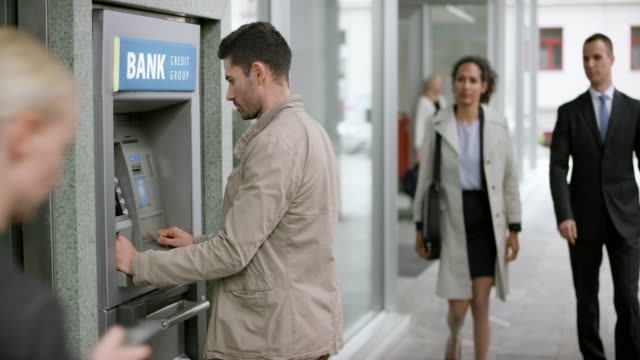 Man making a withdrawal from the ATM machine on a busy street
