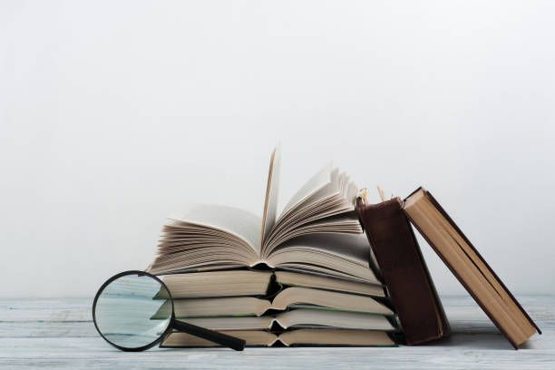 istock Open book, hardback colorful books on wooden table. Magnifier. Back to school. Copy space for text. Education business concept 690053584