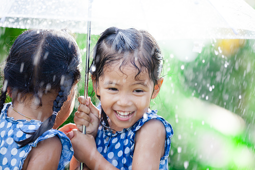 Two happy asian little girls with umbrella having fun to play with the rain together