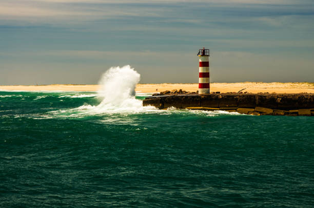 Small lighthouse in the face of a great wave. In the foreground greenish water, second lantern and wave.