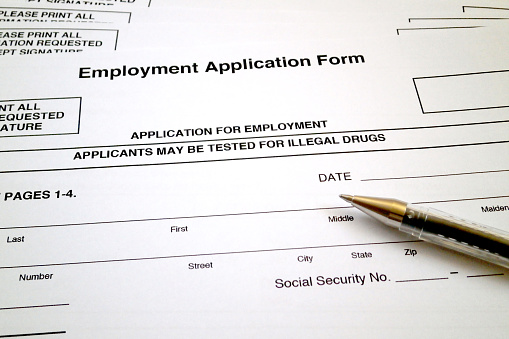 A ballpoint pen on the top of an Employment Application Form specifying that applicants may be tested for illegal drugs.