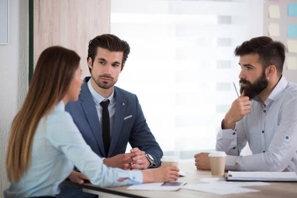 istock Team of three business people sitting at the table with several documents and discussing important questions 690111388