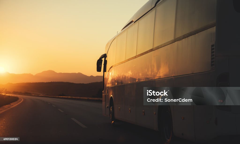 White bus driving on road towards the setting sun Bus Stock Photo