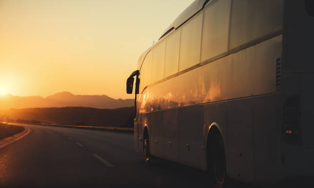 White bus driving on road towards the setting sun stock photo