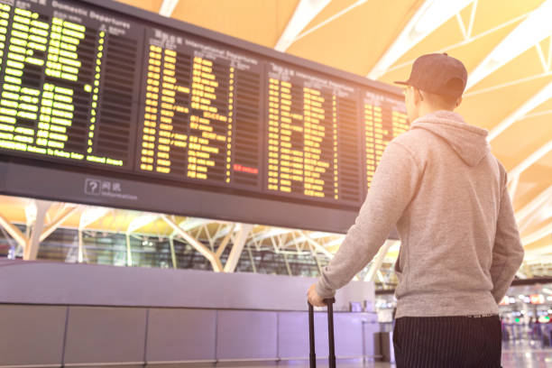 Passenger looking at flights information board in airport terminal stock photo