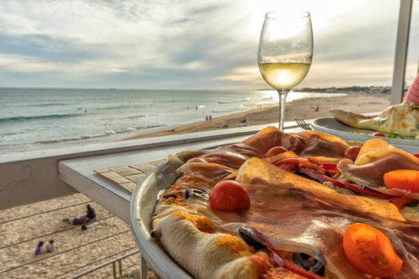pizza maison avec jambon tomate olives et poivrons avec verre de vin blanc et la plage au coucher du soleil en arrière-plan - chianti region photos et images de collection