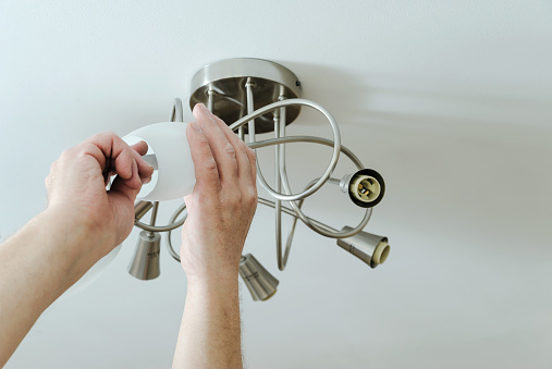 Electrician's hands are installing a LED light bulb in a lamp.