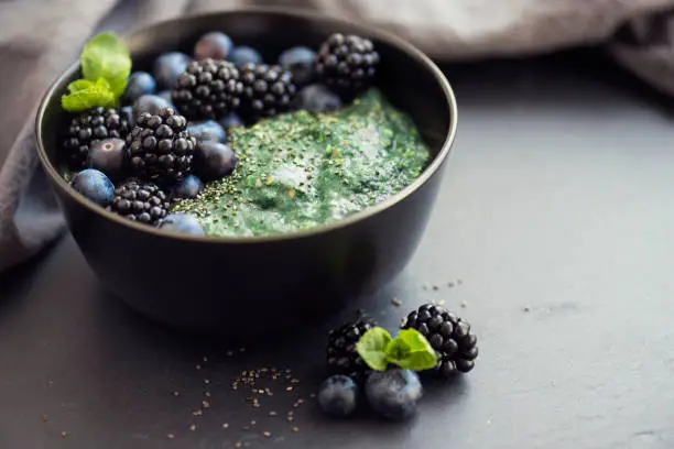 Healthy organic breakfast spirulina porridge topped with blackberries, blueberries, mint leaves, chia and flax seed
