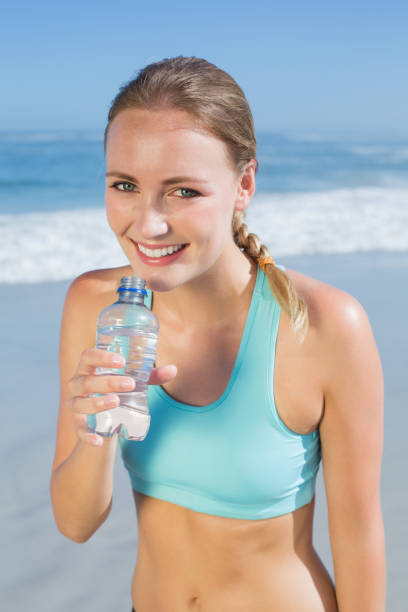istock Fit woman standing on the beach taking a drink 690184054