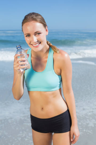 istock Fit woman standing on the beach taking a drink 690184068