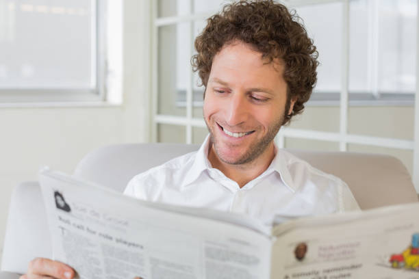 istock Smiling man reading newspaper at home 690191174