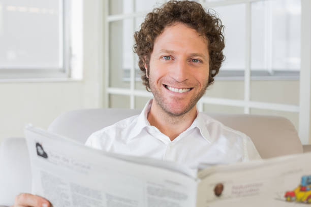 istock Smiling man reading newspaper at home 690191178