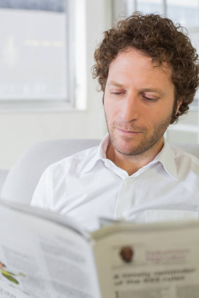 istock Young man reading newspaper at home 690191186